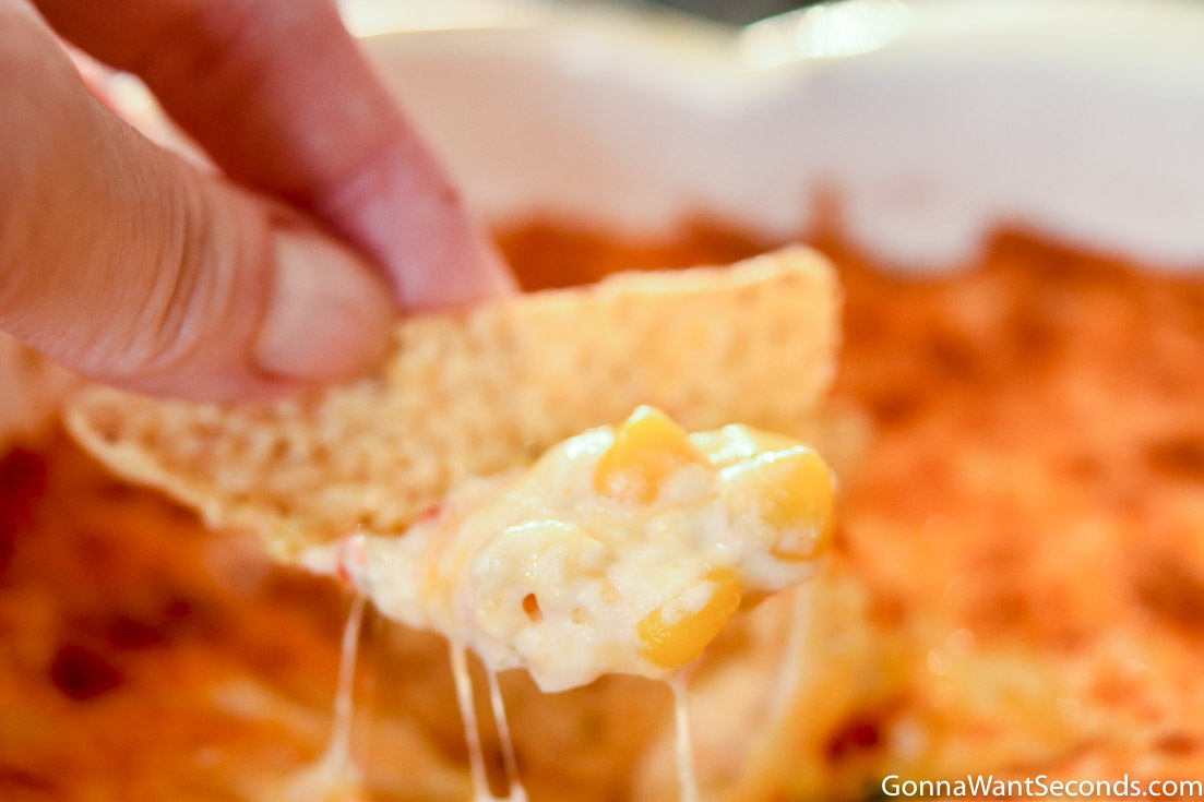 Hand holding a tortilla chip with cheesy hot corn dip recipe