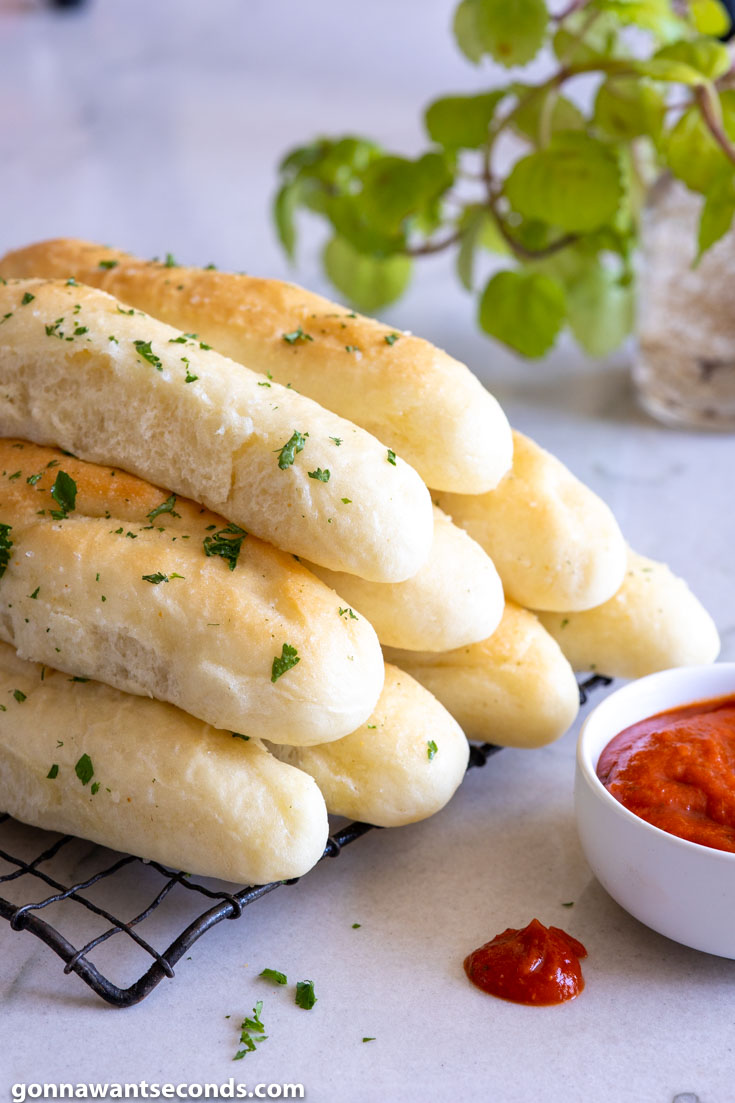 Olive Garden Breadsticks piled on top of each other with dipping sauce on the side