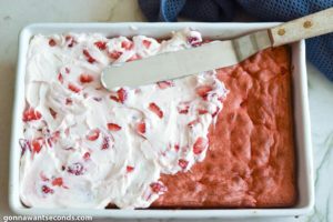 How to make strawberry jello cake, spreading the strawberry buttercream frosting on top of the cake