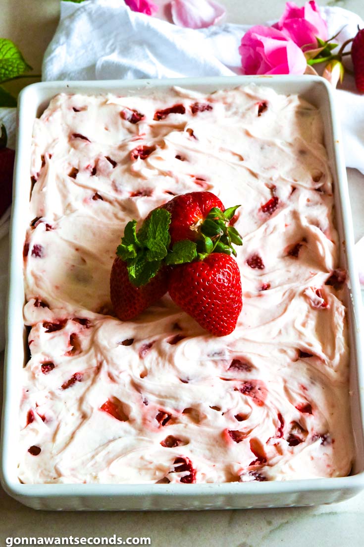 strawberry jello cake with buttercream frosting, topped with fresh strawberries and mint sprigs, in a baking dish