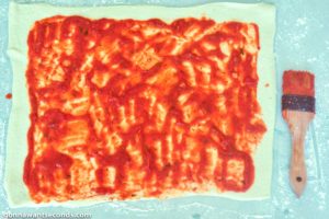 How to make Pizza Pinwheels, spreading sauce on crust