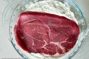 How to make Swiss Steak, dredging the steak in flour