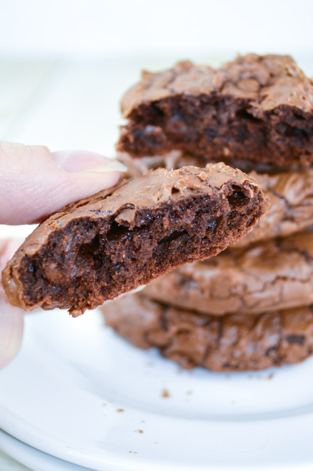 Close up holding half of Brownie Cookies with cookies stack on top of each other on a plate at the back