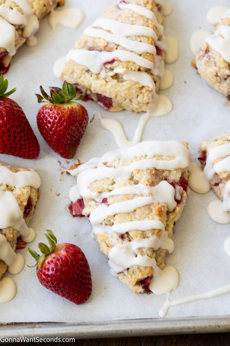 fresh strawberry scones drizzled with glaze, on a baking sheet