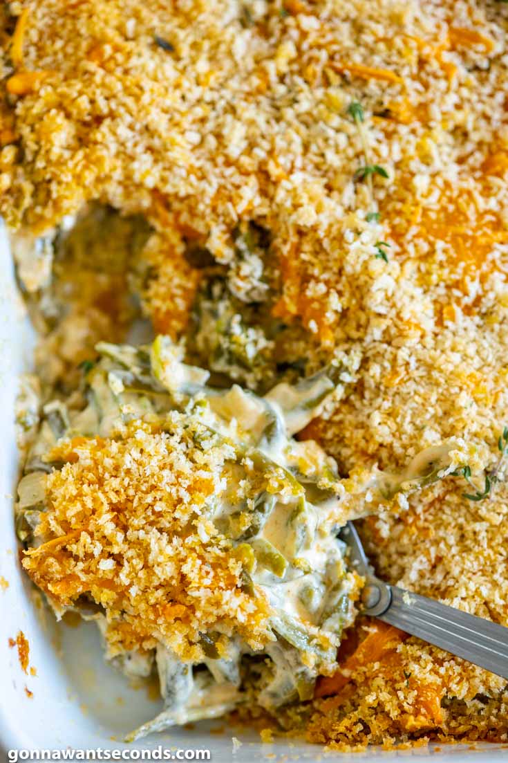 Serving spoon in green bean casserole with cheese and breadcrumbs