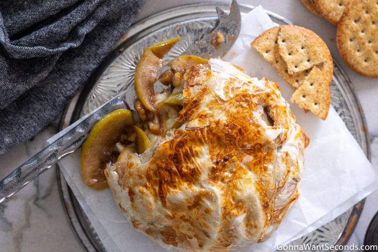 puff pastry baked brie, with cracker on the side, showing apples and walnuts inside