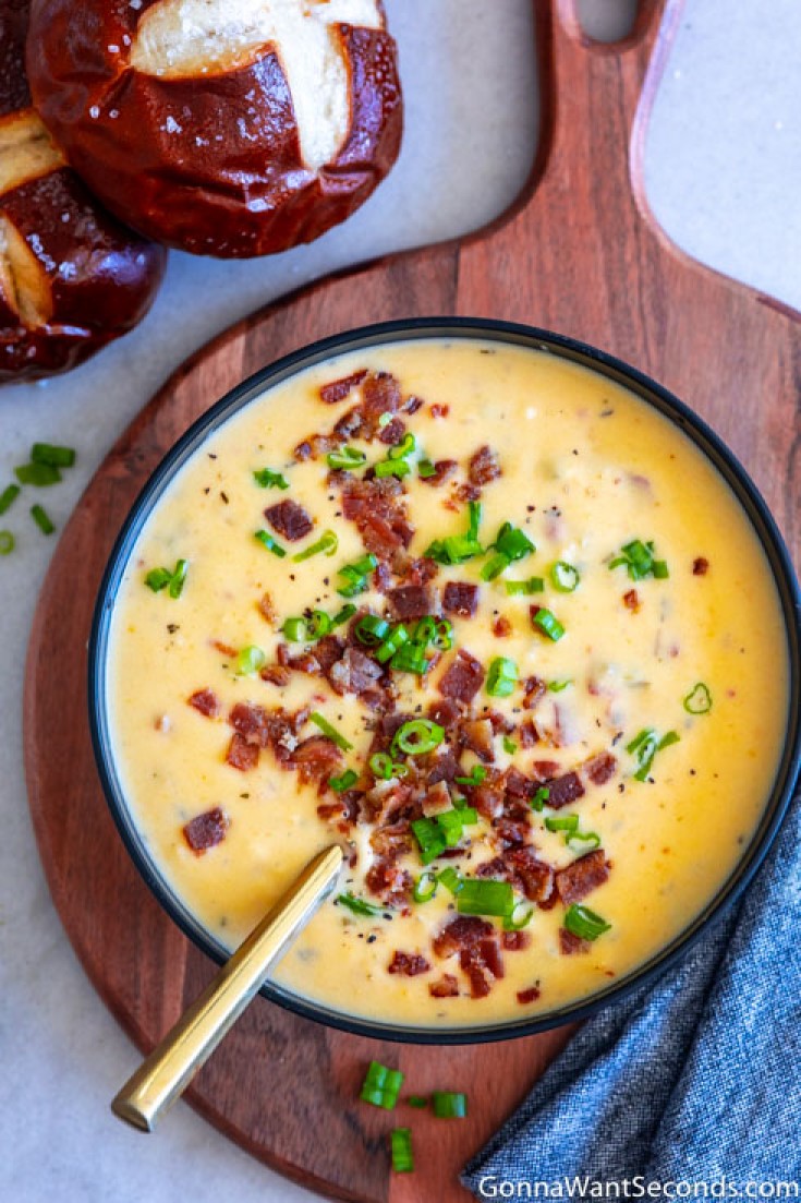 creamy beer cheese soup topped with bacon and green onions in a bowl, with bread rolls on the side