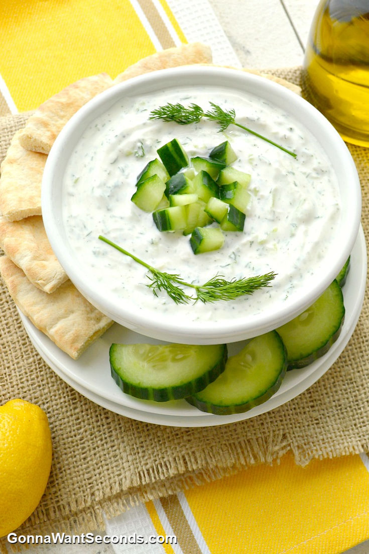 tzatziki sauce topped with chopped cucumber and dill with cucumber and pita slices around