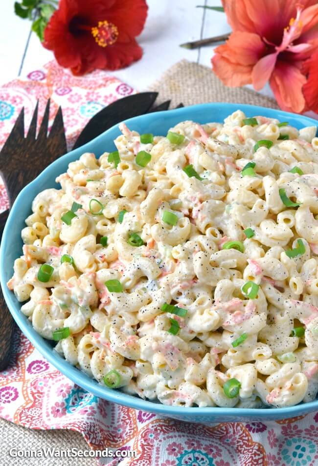 classic hawaiian macaroni salad in a blue bowl with wooden serving fork and gumamela on the table