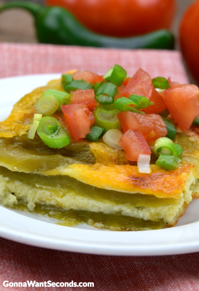 A slice of best chili relleno casserole topped with tomatoes and green onions on a plate 