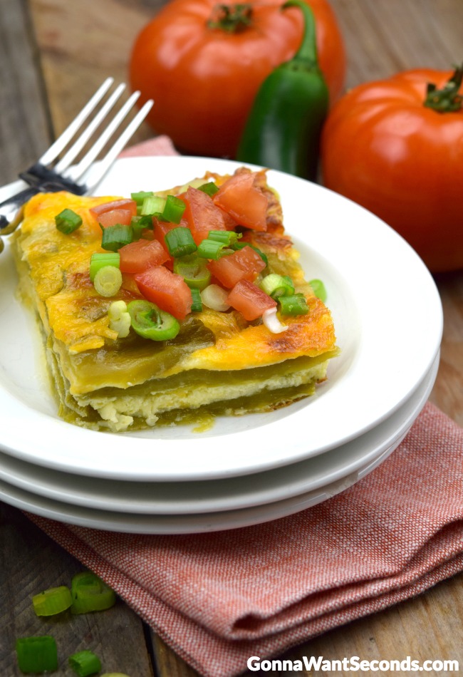 A slice of best chili relleno casserole topped with tomatoes and green onions on a plate 