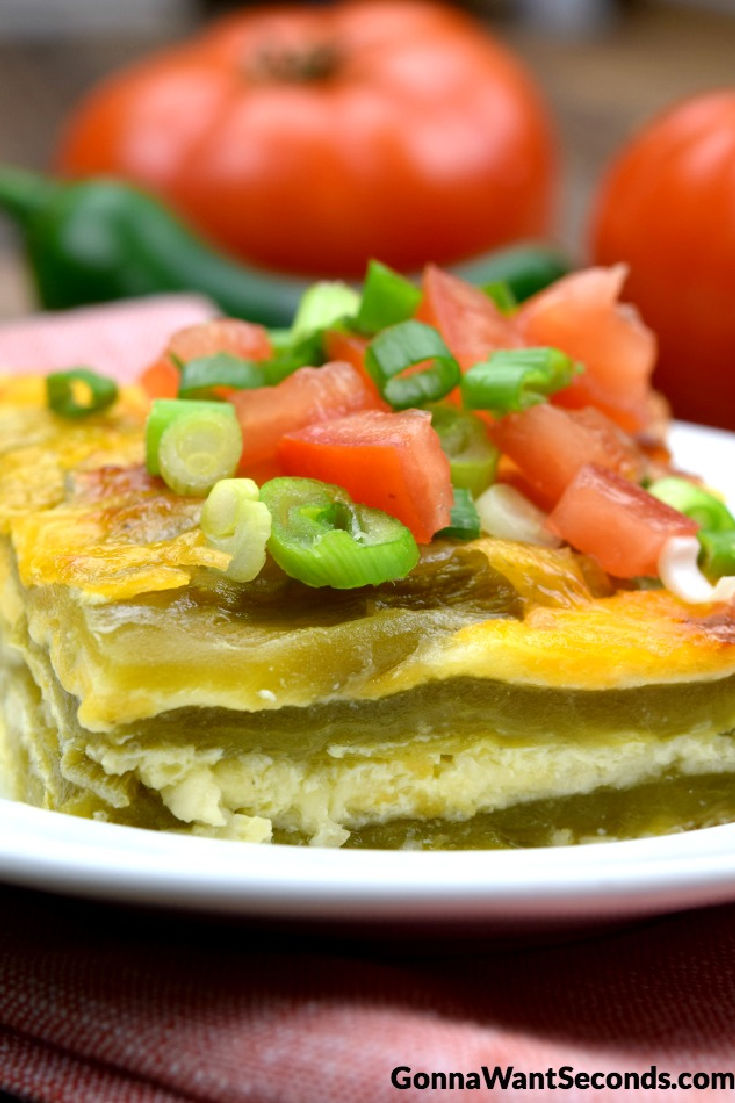 A slice of chili relleno casserole topped with tomatoes and green onions on a plate 