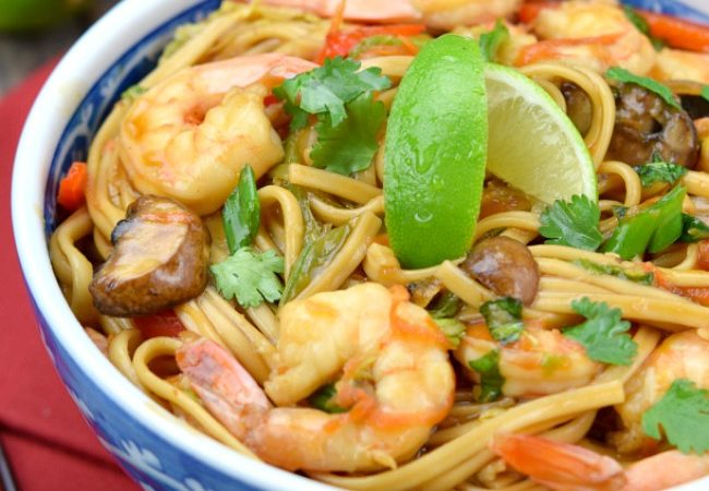 Shrimp Lo Mein topped with sliced limes, in a blue porcelain bowl