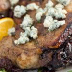 Stuffed Pork Chop topped with bleu cheese, garnished with fresh orange on a white plate