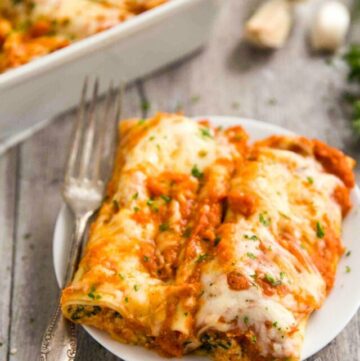 Cannelloni on a plate with fork on the side and a casserole at the back