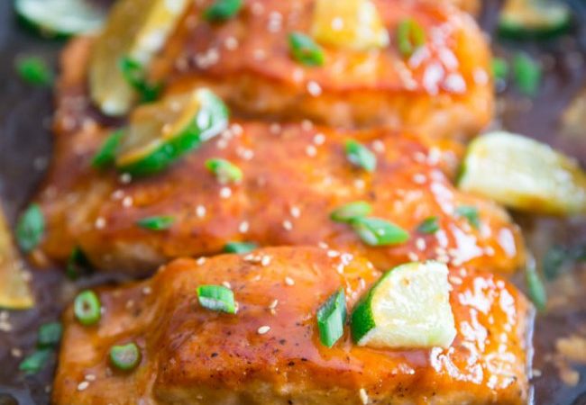 Honey Glazed Salmon on a Platter Garnished with Sliced Limes, Chopped Green Onions, and Sesame Seeds