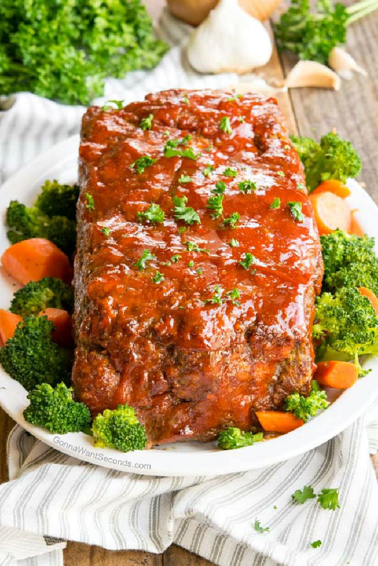 Whole alton brown meatloaf with veggies around it on a serving platter