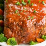 Alton Brown Meatloaf on a white platter surrounded by broccoli and carrots