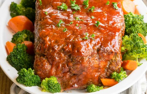 Alton Brown Meatloaf on a white platter surrounded by broccoli and carrots