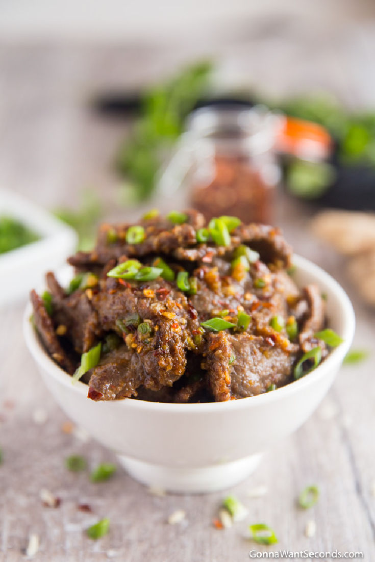 spicy hunan beef sprinkled with green onions and red chili flakes in a white bowl