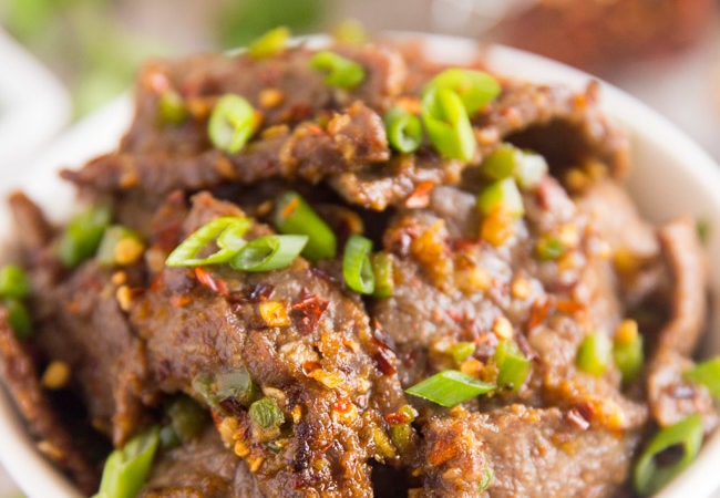 Hunan Beef sprinkled with green onions and red chili flakes in a white bowl