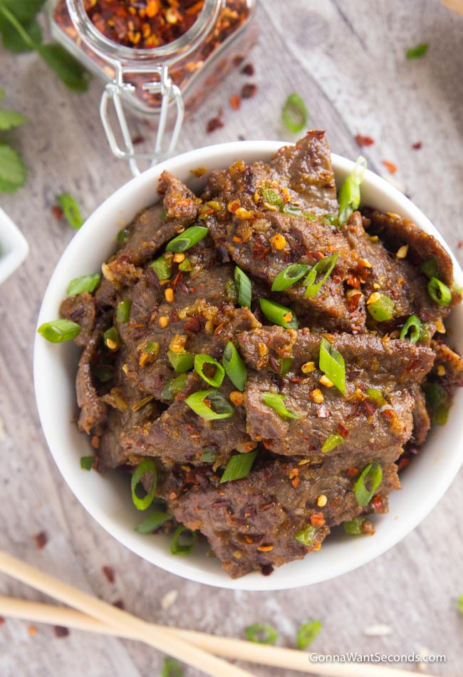 Hunan Beef sprinkled with green onions and red chili flakes in a white bowl