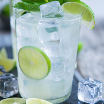 A highball glass filled with Lime Rickey, ice, and lime wedges