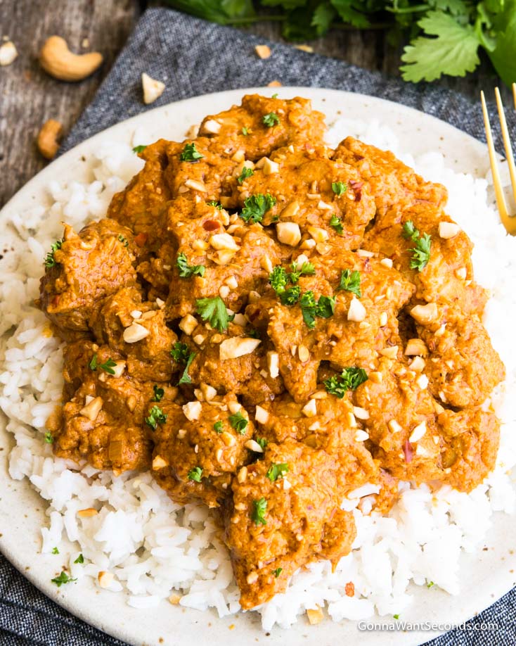 A bowl of rice topped with Butter Chicken garnished with parsley and ground cashews