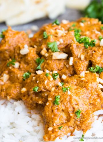 A bowl of rice topped with Butter Chicken garnished with parsley and ground cashews