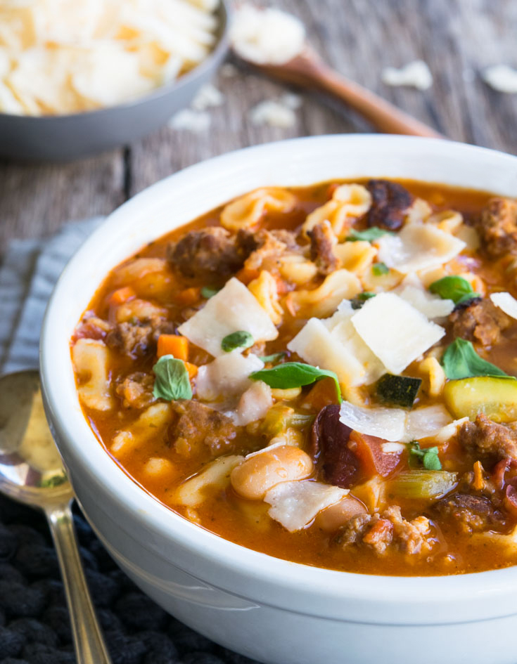 Italian Sausage Soup garnished with basil and cheese, in a bowl