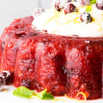 cranberry pineapple jello salad with lemon cream cheese toppings in the center, garnished with sugared cranberries, on a cake stand