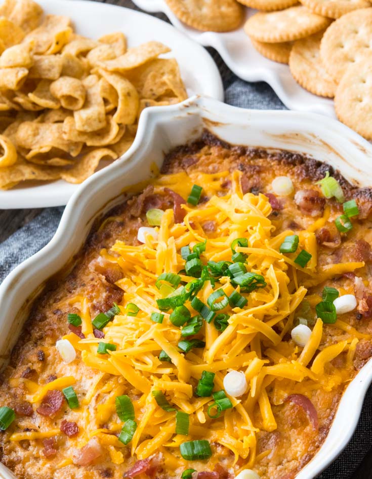 Crack Dip in a 2-quart baking dish topped with shredded cheese and green onions, with chips and crackers on the side