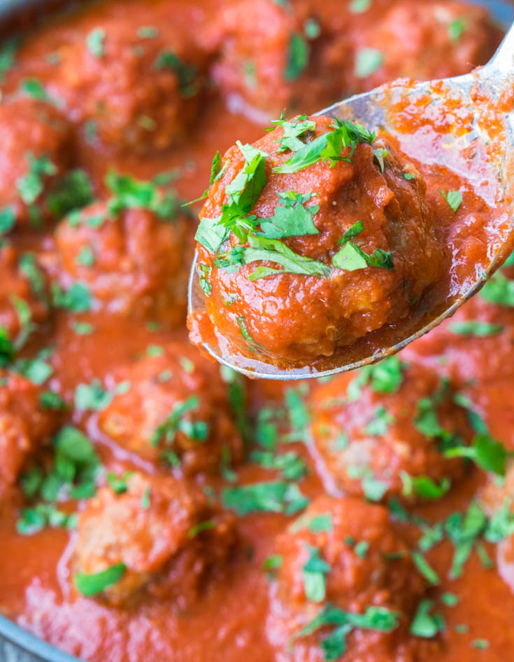 Mexican Meatballs being scooped from a pan full of meatballs and tomato sauce