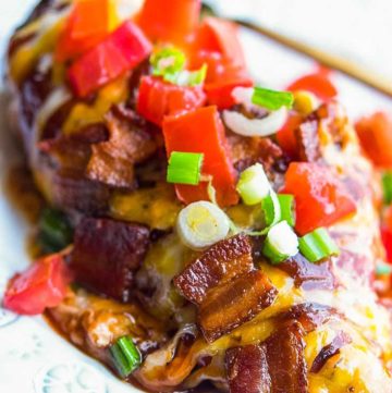 Monterey Chicken topped with melted cheese, chopped bacon, green onions, and tomatoes, on a plate