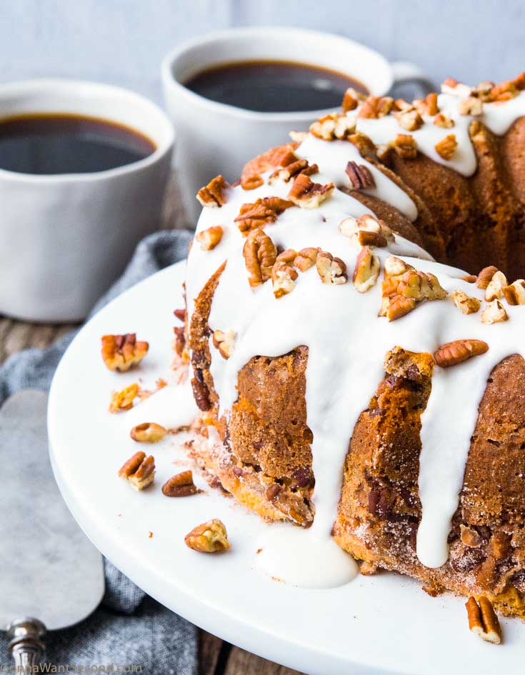 Sour cream coffee cake with glaze on top, garnished with chopped pecans. With two cups of coffee on the side