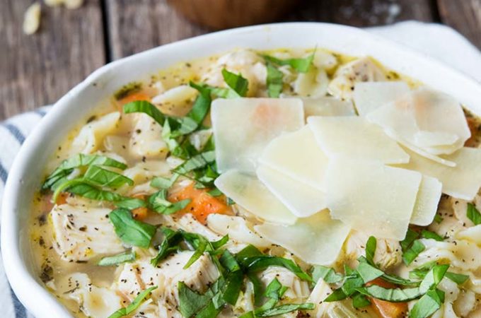 Italian Chicken Soup in a bowl, topped with shaved parmesan cheese and parsley