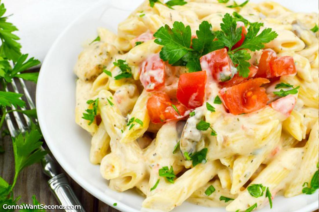 Chicken Alfredo topped with chopped tomatoes and parsley on a white plate