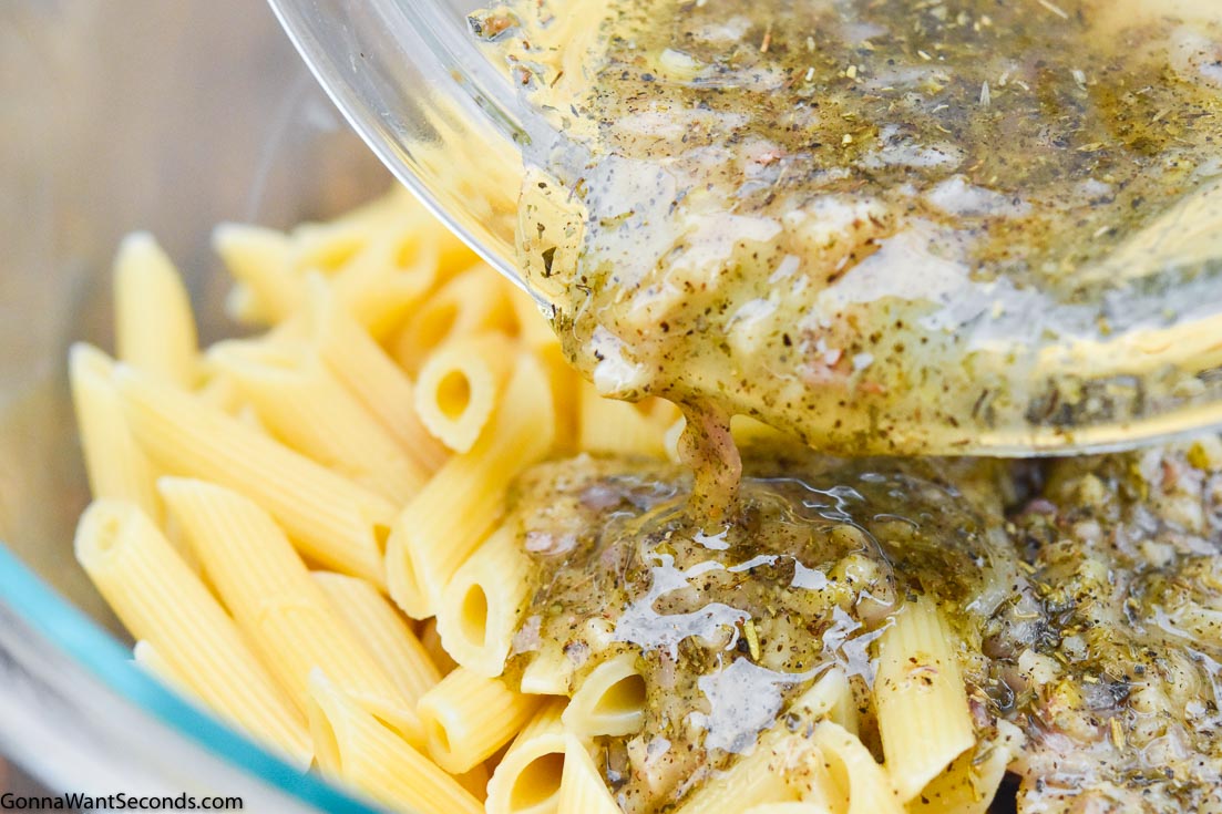 Pouring Mediterranean pasta salad dressing over pasta