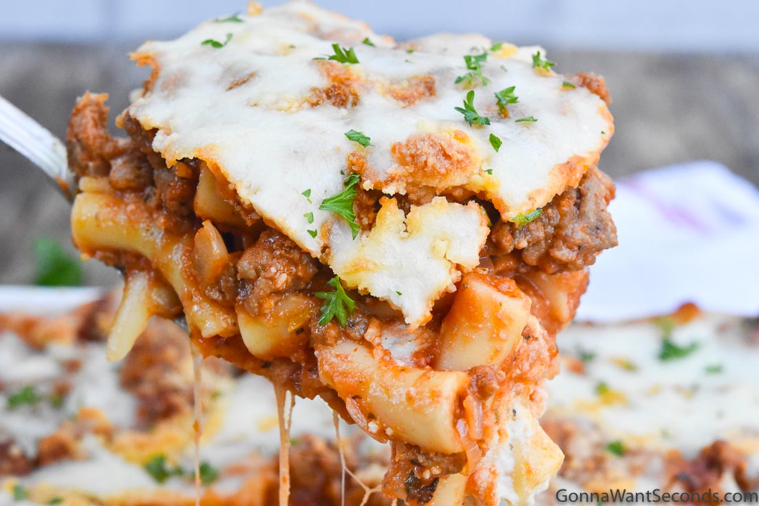 Scooping baked ziti with meat from a casserole dish