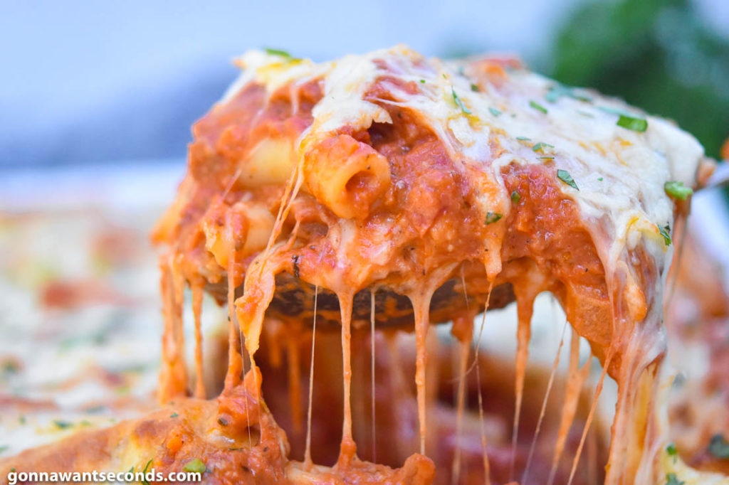 Tour the flavors of Italy with a ziti pasta recipe featuring plenty of creamy melted cheese, perfectly cooked ziti pasta and lots of fragrant herbs. #ZitiPasta #ZitiPastaRecipes wooden ladle scooping baked ziti with Italian sausage from the casserole dish