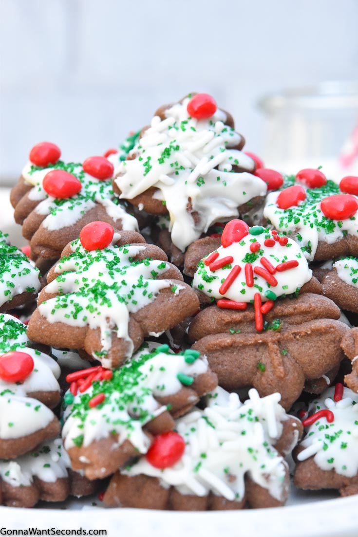 A pile of chocolate spritz cookies in a plate, with a glass of milk at the side