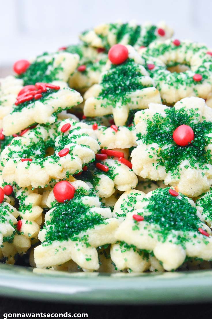 Cream Cheese spritz cookies, decorated with green sugar, red hots, sprinkles, and jimmies, piled on a plate