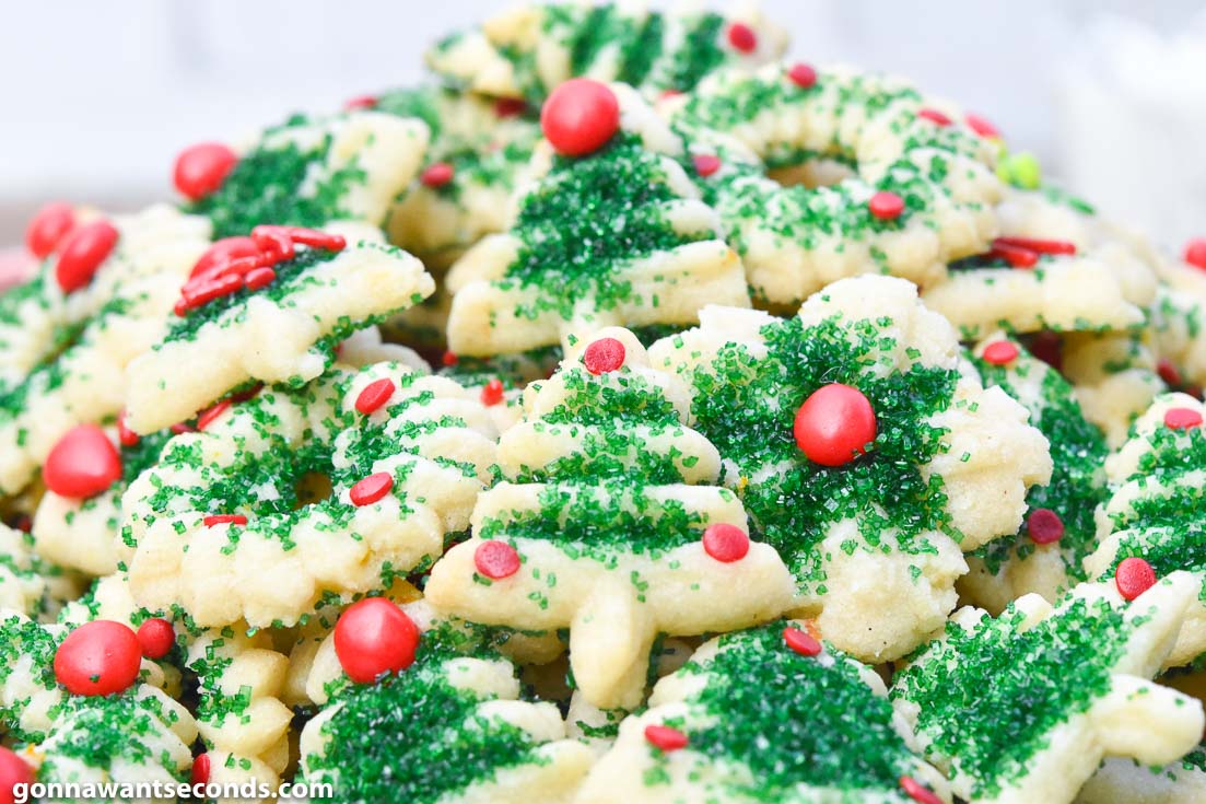 Cream Cheese spritz cookies, decorated with green sugar, red hots, sprinkles, and jimmies, piled on a plate