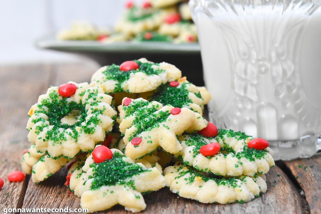 Cream Cheese spritz cookies, decorated with green sugar, red hots, sprinkles, and jimmies,with a glass of milk on the side