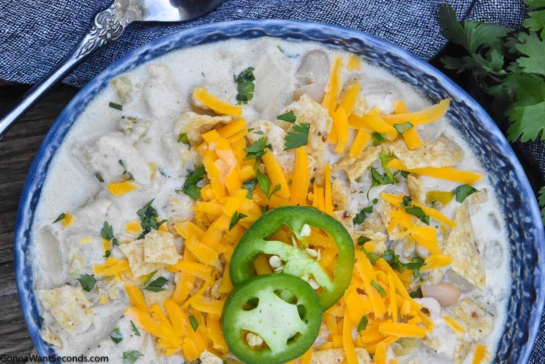 Creamy white chicken chili on a blue bowl, topped with jalapeno and cheese