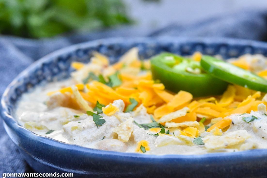 Creamy white chicken chili on a blue bowl, topped with jalapeno and cheese