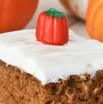 A slice of Pumpkin Bars with Cream Cheese Frosting with pumpkins at the back