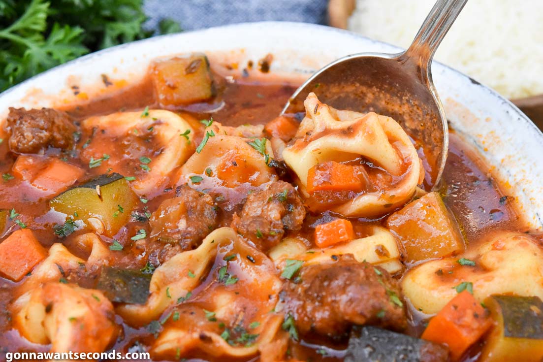 Spoon scooping sausage tortellini soup with zucchini from a bowl