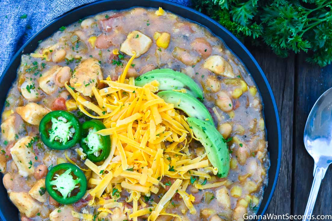White Chicken Chili topped with avocados, shredded cheese, and jalapenos, in a bowl