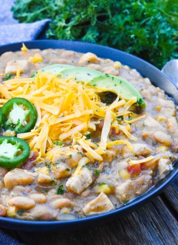 White Chicken Chili topped with avocados, shredded cheese, and jalapenos, in a bowl
